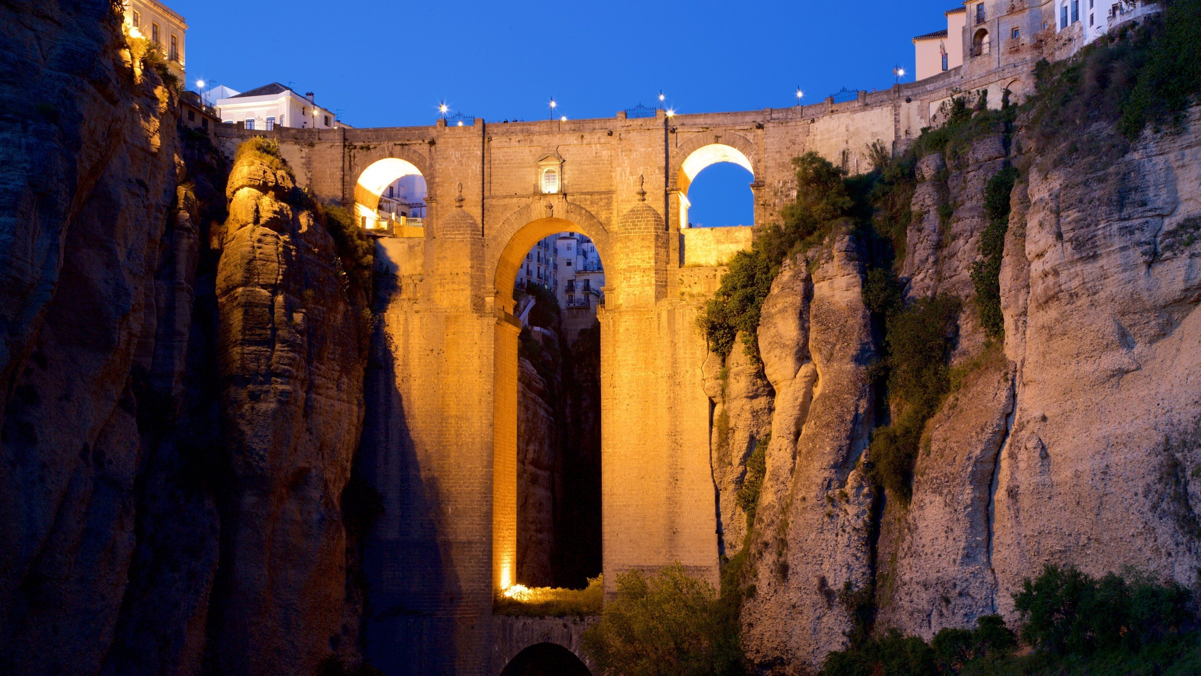 A stone bridge with arches, surrounded by rocky cliffs and buildings.