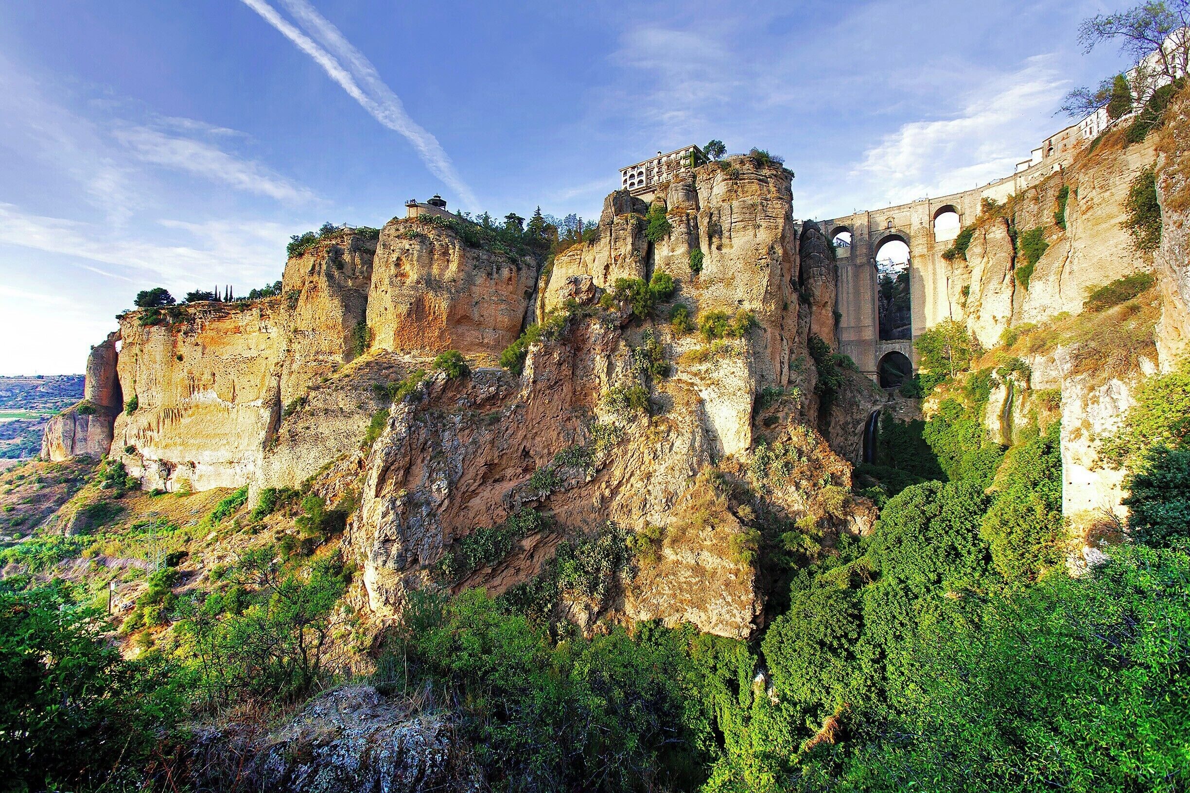A broad view of Ronda's western face and iconic bridge. For a sense of scale, remember that the bridge crosses 98M (320ft) above the Guadalevín River.  To the right of the bridge you'll find the charming old quarter, while to the left you'll find the new town (which is still hundreds of years old).

For this particular view you'll have to make your way down a long pathway to the Puerta de los Molinos (a deteriorating city gate). The best time to make the hike is late afternoon or early evening, when the weather is cool and the bridge is bathed in sunlight. The path starts at the Plaza Maria Auxiliadora.