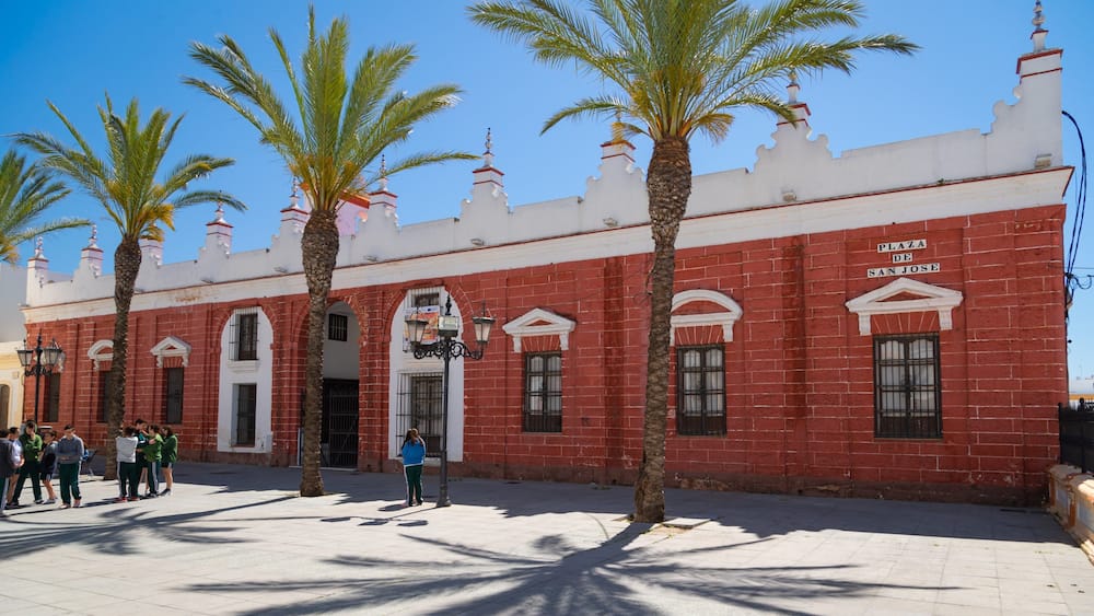 Plaza de San Jose mit roten Backsteingebäuden, Palmen und blauem Himmel.