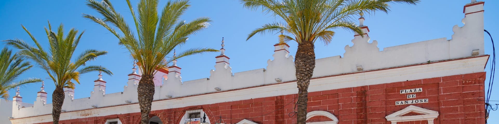 Plaza de San Jose with red brick buildings, palm trees, and a clear blue sky.