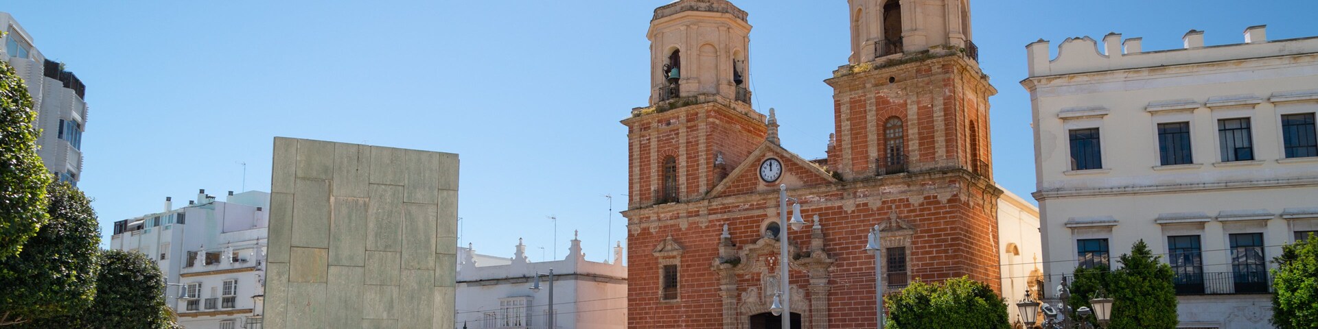 A historic church with two towers, a square with people and a statue, and modern buildings in the background.