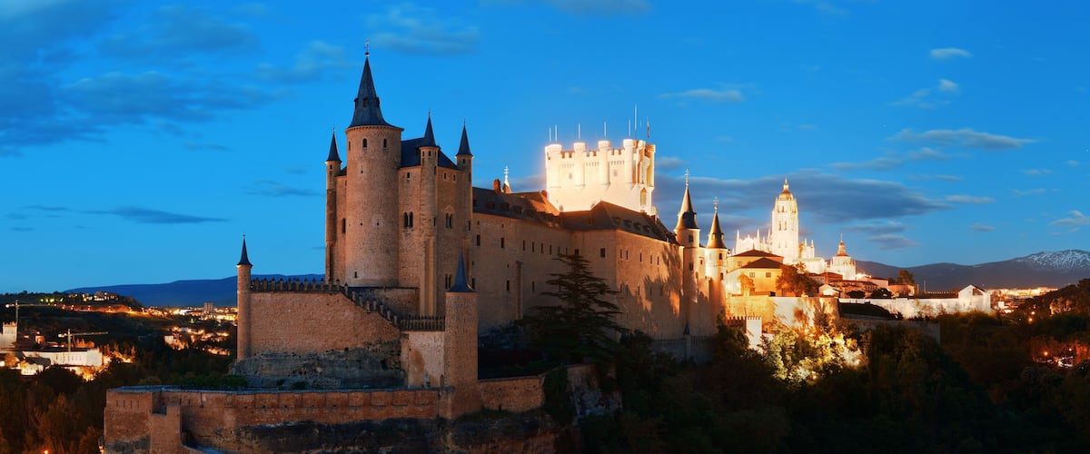 A historic castle with multiple towers and a prominent white building in the background.