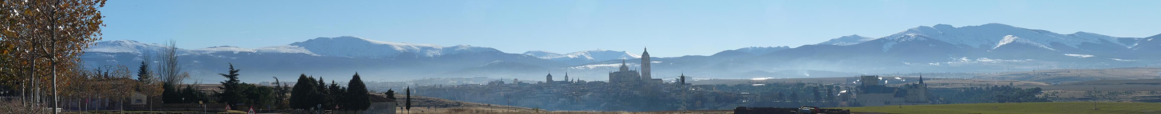 A mountainous landscape with a city in the valley, snow-capped peaks, and a clear sky.