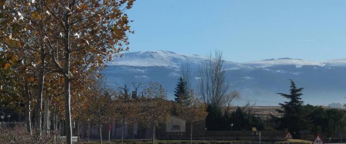 A mountainous landscape with a city in the valley, snow-capped peaks, and a clear sky.