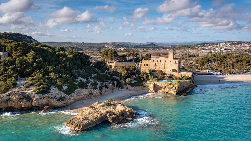 A coastal town with a prominent castle on a hill, clear turquoise waters, and a sandy beach.