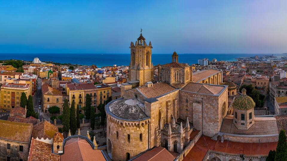 A coastal cityscape with historic architecture, including a prominent church with a bell tower and a cathedral with a dome.