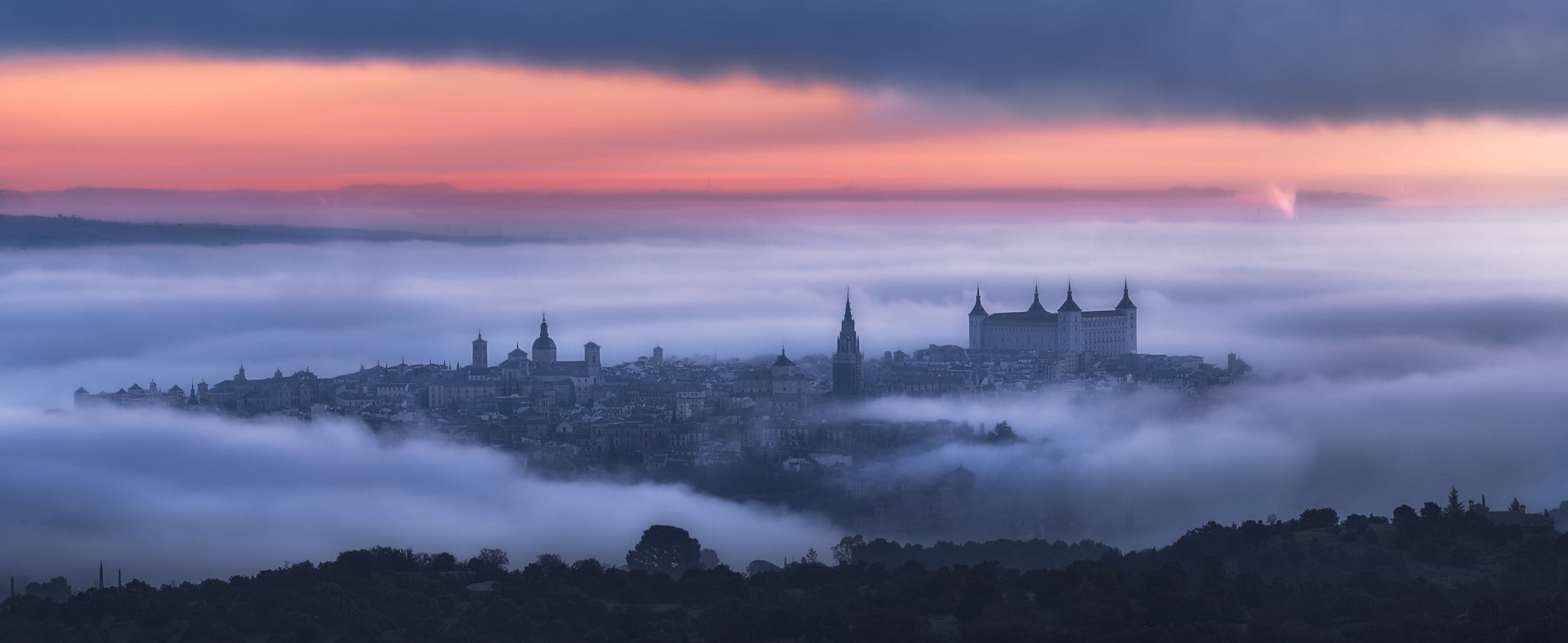 Aerial view of ancient town and medieval Alcazar de Toledo palace in mist in colorful daybreak
