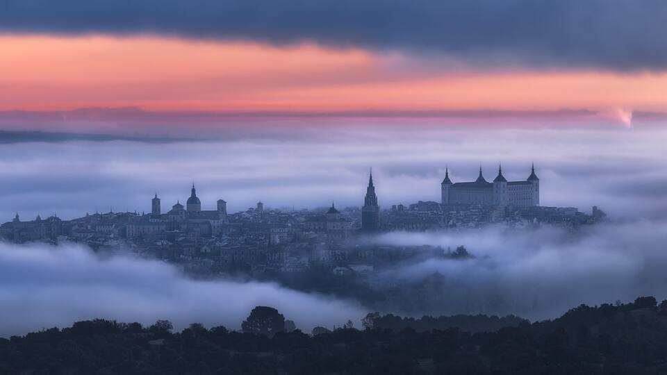 Aerial view of ancient town and medieval Alcazar de Toledo palace in mist in colorful daybreak