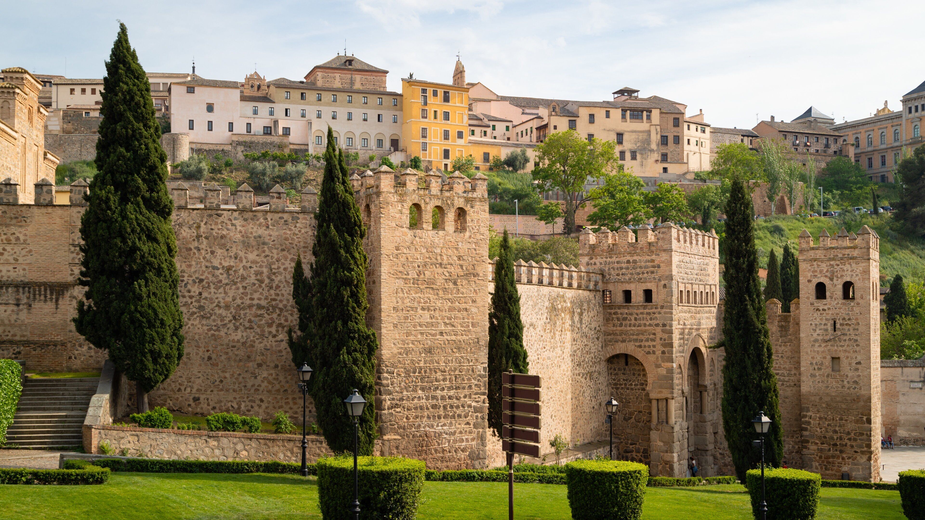 A historic stone wall with towers, surrounded by well-maintained hedges and a clear sky.