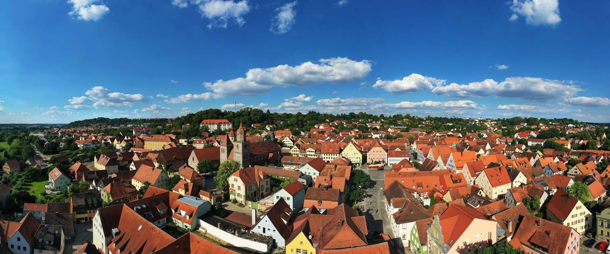A town with red-roofed buildings, a church, and green hills in the background.