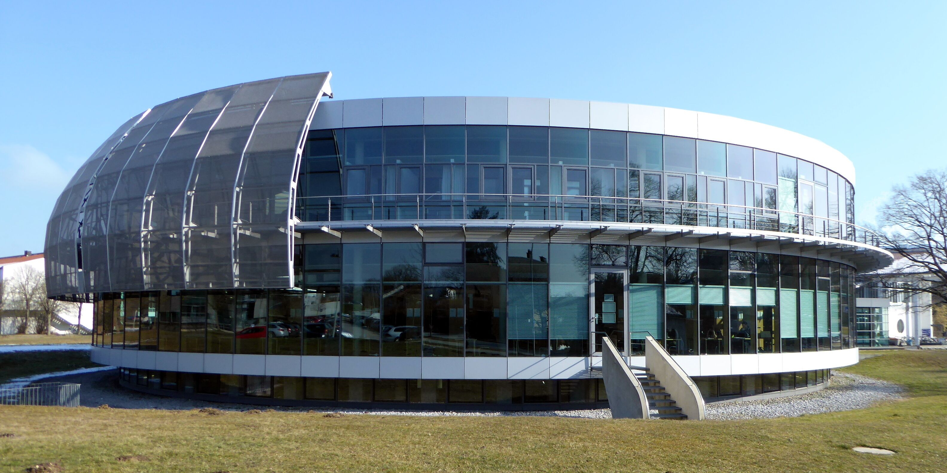 Un edificio moderno con fachada de vidrio curva y una amplia estructura de techo transparente.