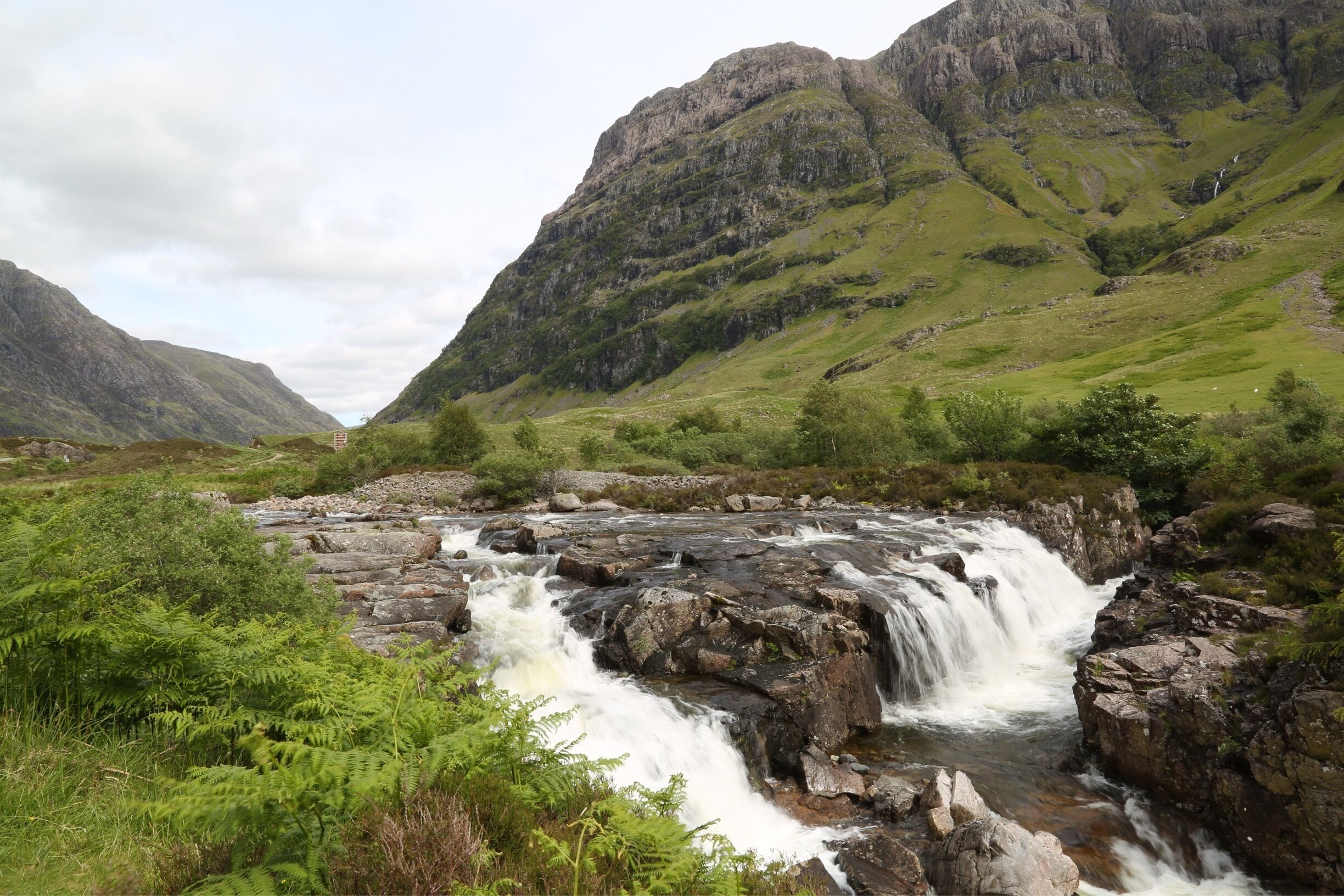 A waterfall in a mountainous area with lush greenery and rocky terrain.