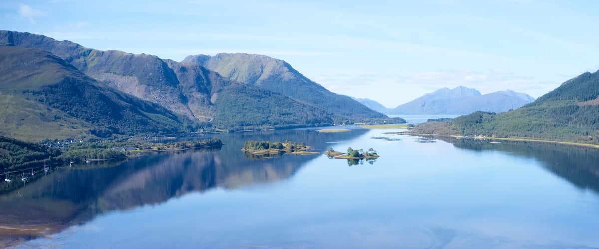 A calm lake surrounded by mountains and a small island with boats.