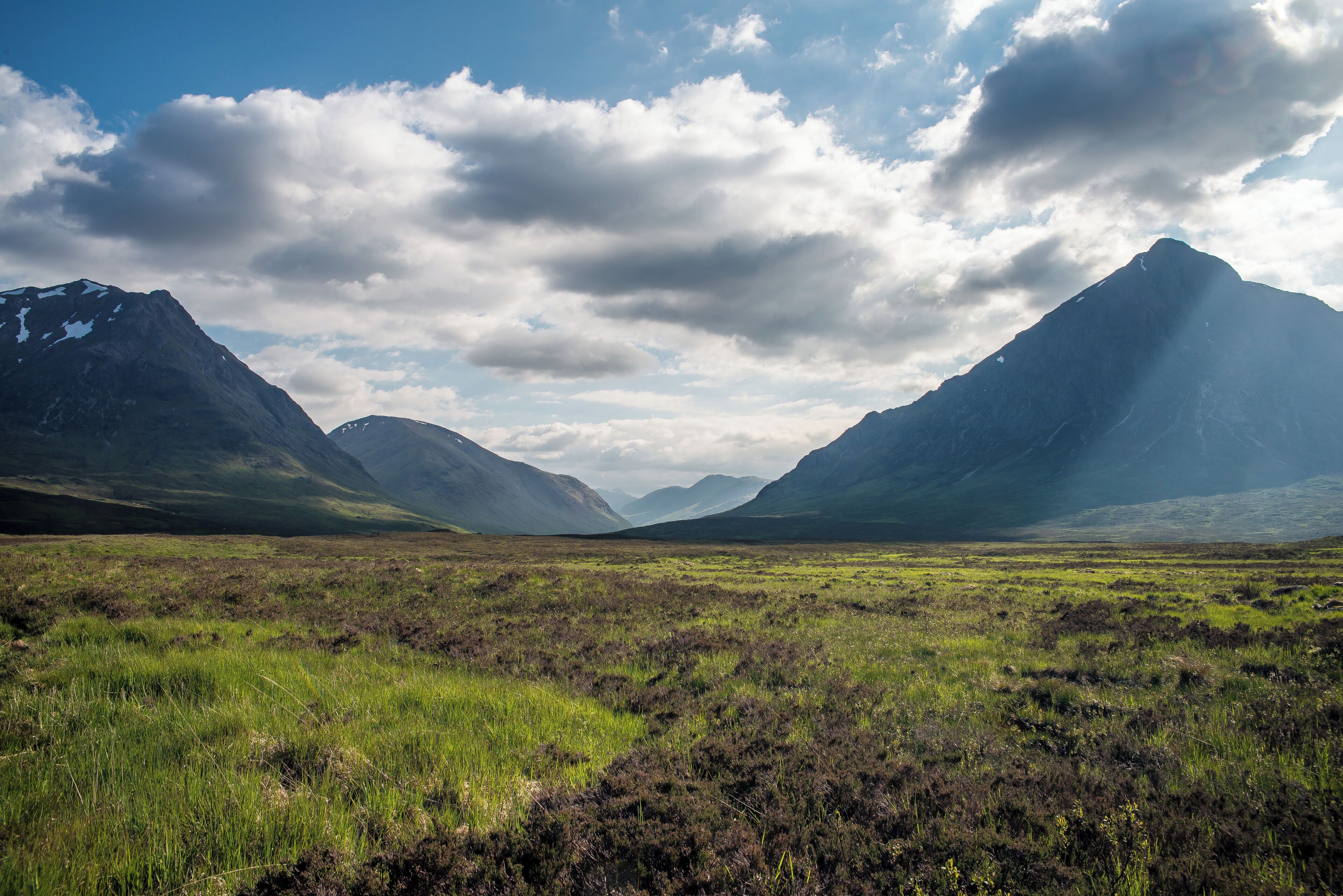 A mountainous landscape with a grassy field and a cloudy sky.