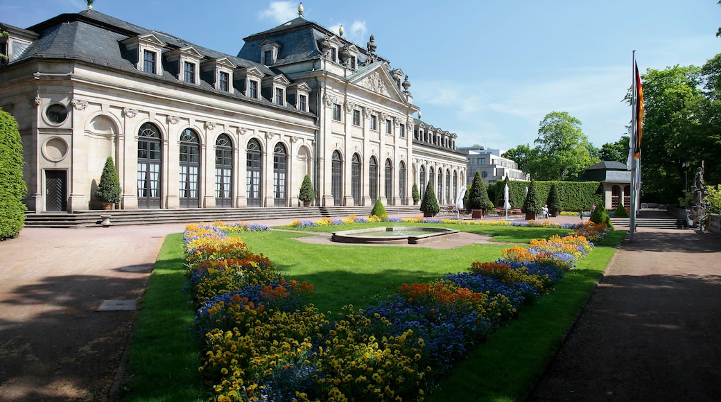 A classical building with a symmetrical facade, a central courtyard with flower beds, and a flagpole.