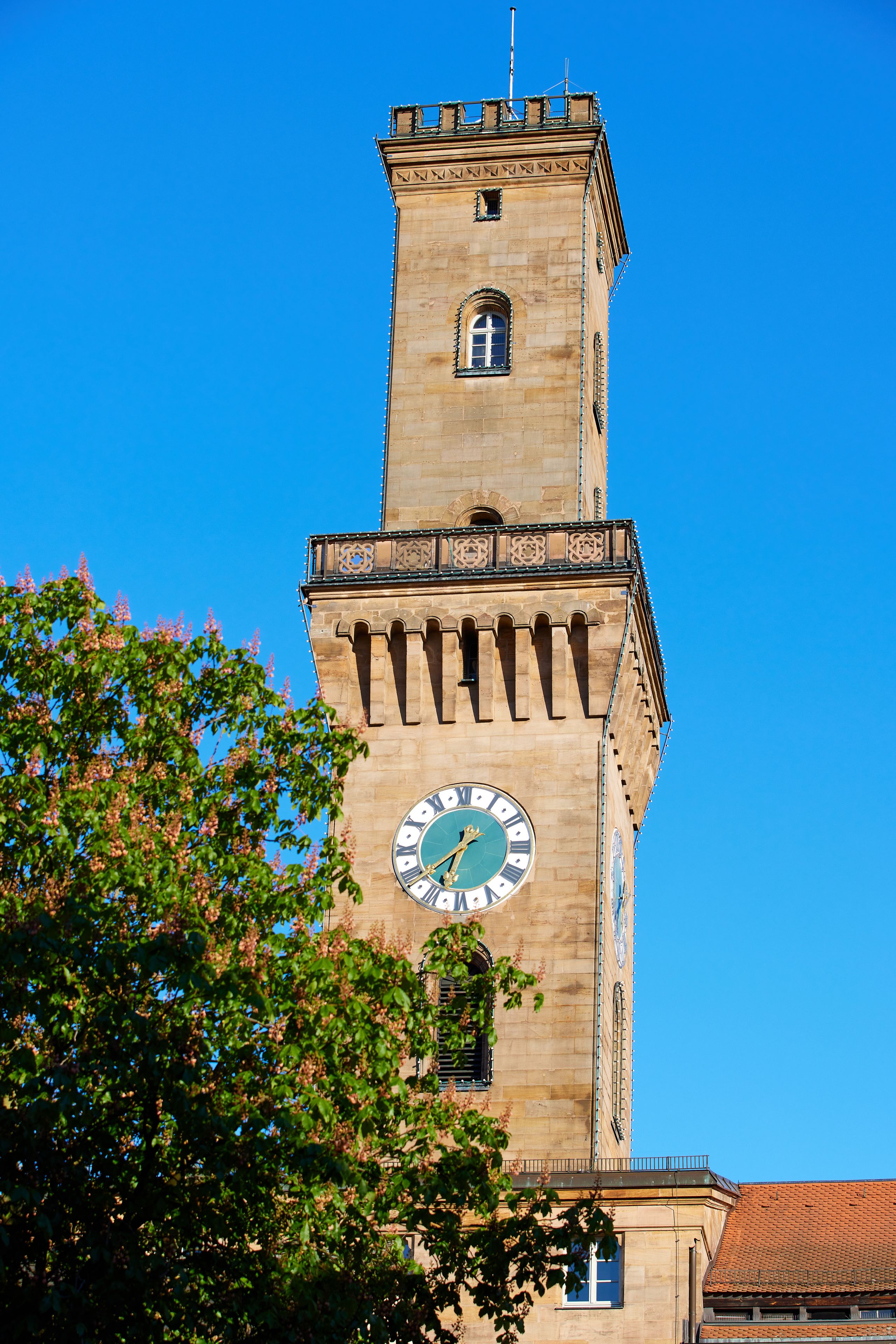 Ein hoher Turm mit einer Uhr, umgeben von blauem Himmel und viel Grün.