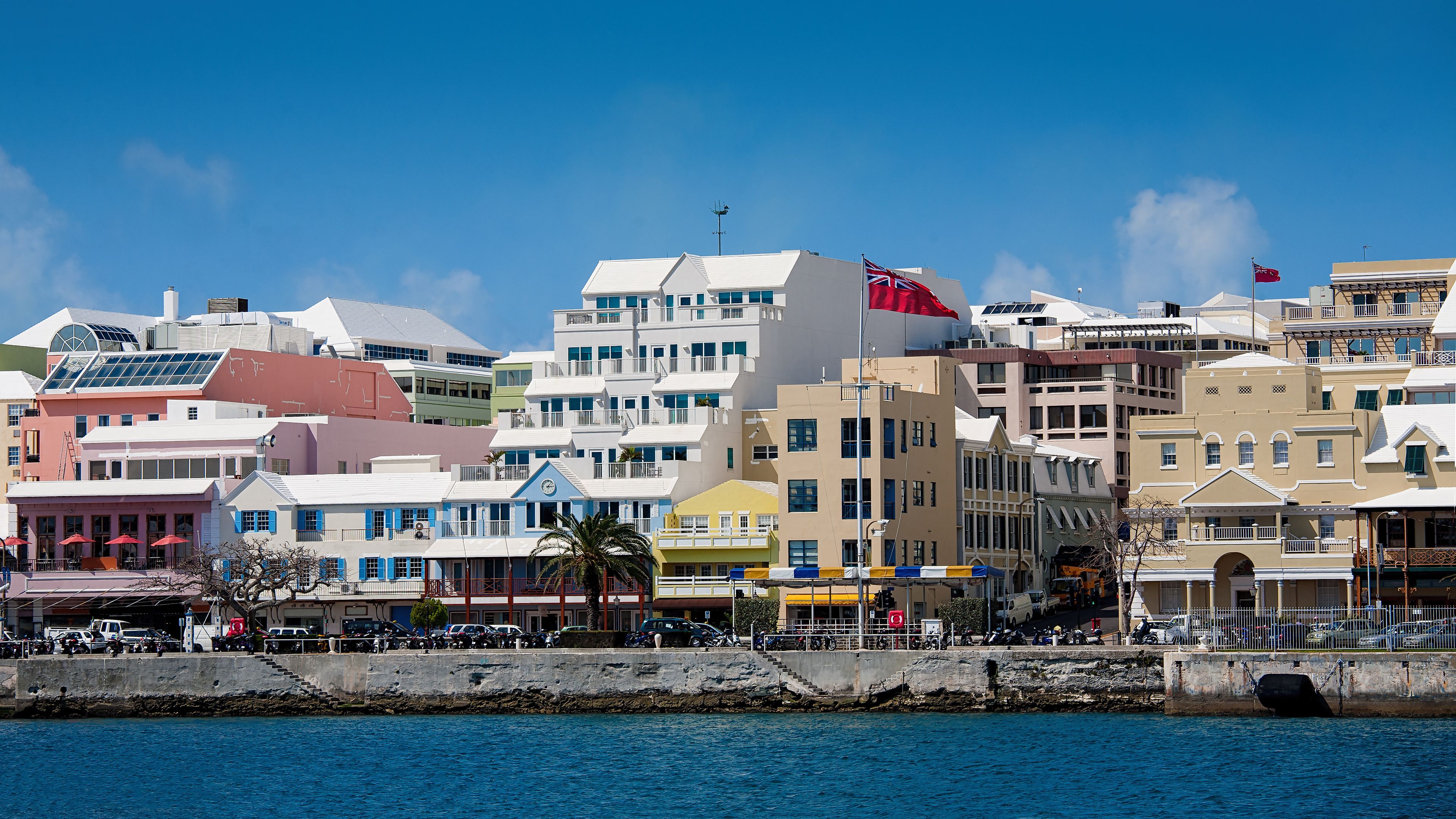 A coastal cityscape with colorful buildings, a clear blue sky, and a calm sea.
