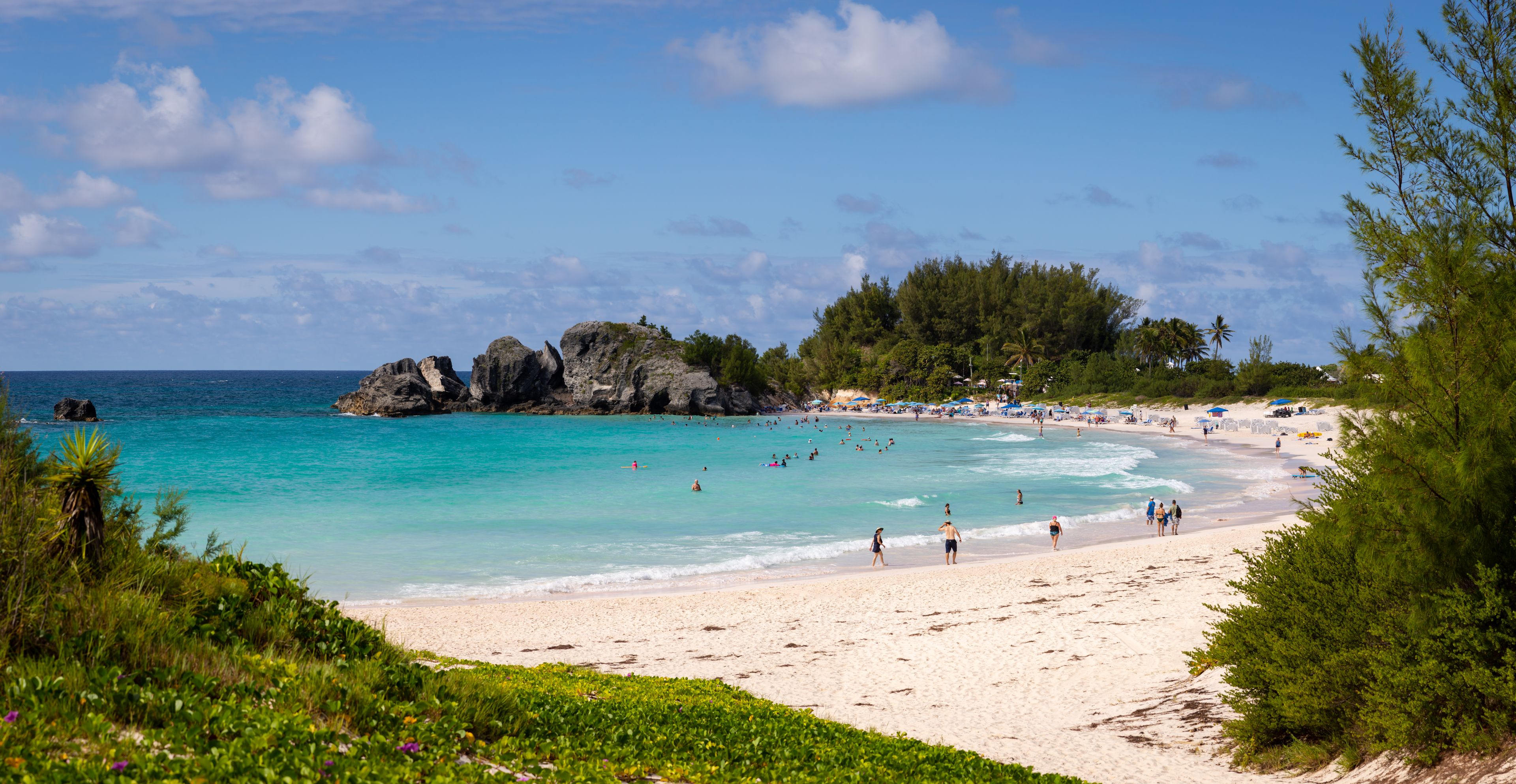 A beach with clear turquoise waters, a rocky outcrop, and lush greenery.