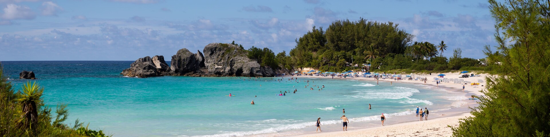 Una playa con aguas turquesas cristalinas, un promontorio rocoso y abundante vegetación.