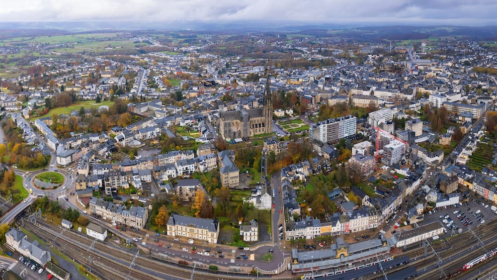 Une vue aérienne d’une ville avec une église imposante, des voies ferrées et des champs verdoyants environnants.