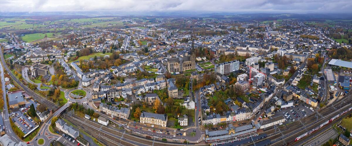 An aerial view of a city with a prominent church, railway lines, and surrounding green fields.