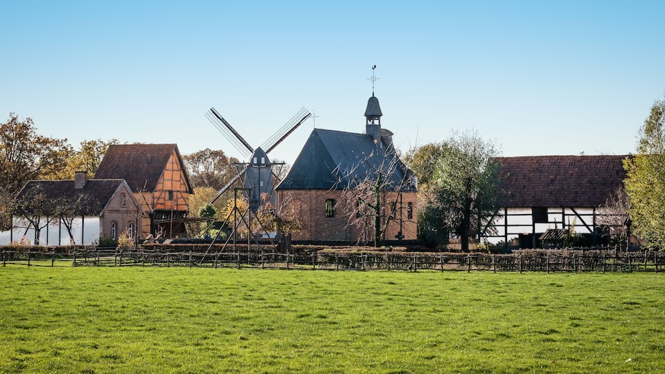 A windmill, a church, and a thatched-roof building in a rural setting.