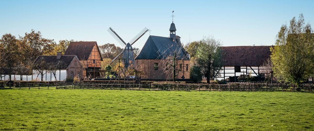 A windmill, a church, and a thatched-roof building in a rural setting.