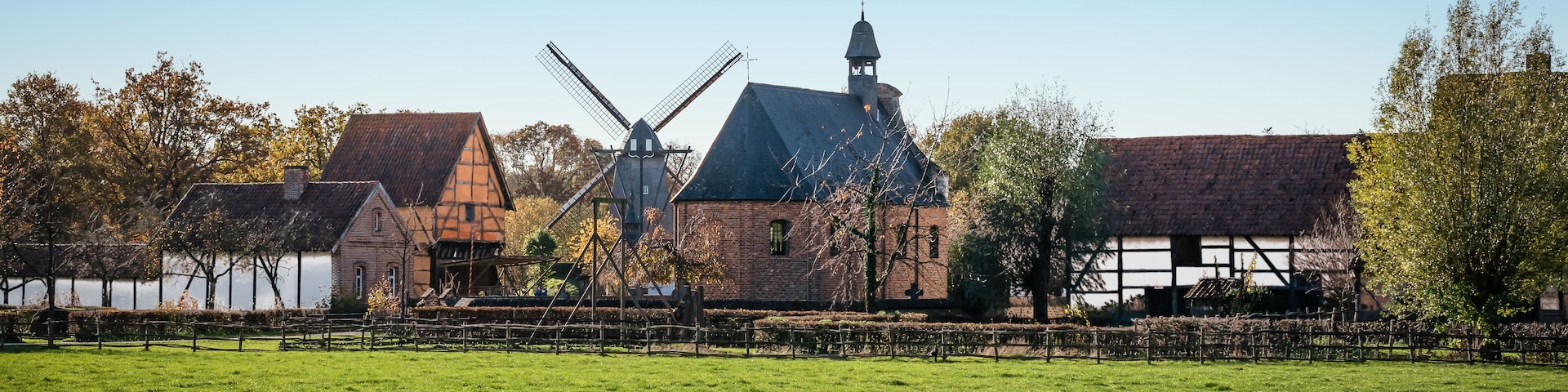 A windmill, a church, and a thatched-roof building in a rural setting.