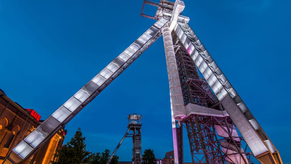 A tall, metallic structure with a sloped roof, likely a part of an amusement park ride, set against a twilight sky.