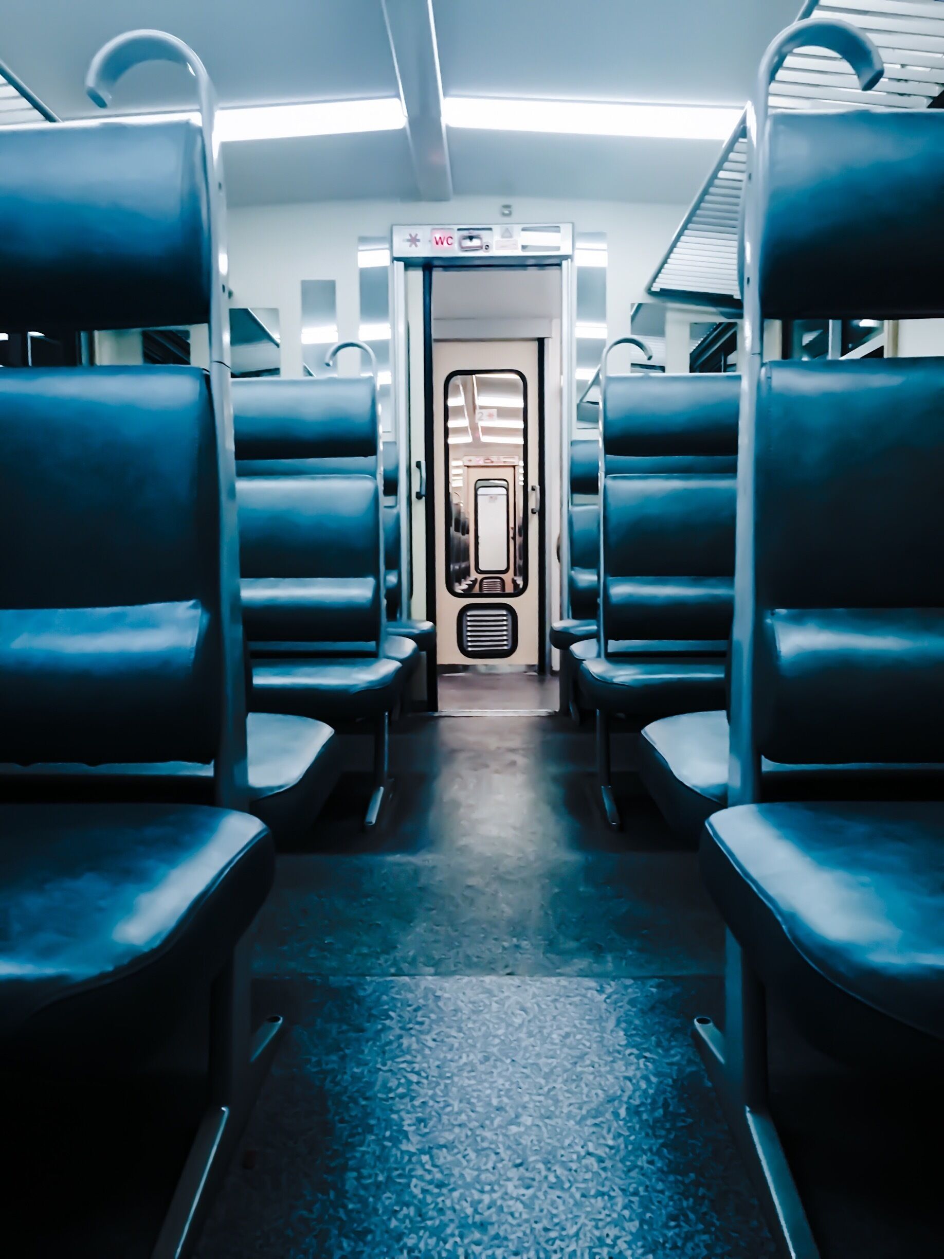 Interior de un tren con asientos azules y una puerta que indica un baño.