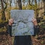 Una persona sosté un mapa topogràfic detallat en un bosc.