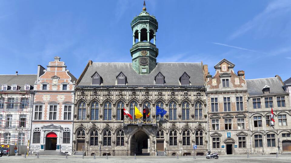 A historic building with a prominent tower, multiple flags, and an arched entrance.