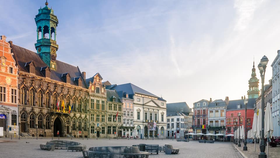 A historic square with cobblestone pavement, a prominent clock tower, and colorful buildings.