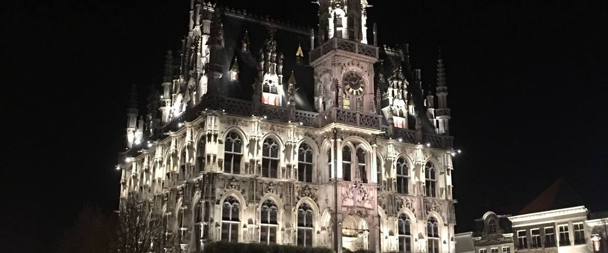 A historic building with intricate architecture and a clock tower, illuminated at night.