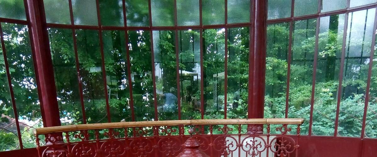 A red metal railing with intricate designs, a central red water spout, and a tiled floor with water puddles.