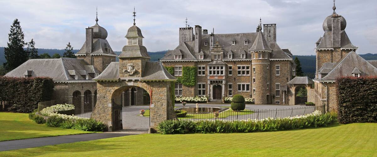 A large, historic stone building with multiple towers and a well-maintained lawn.