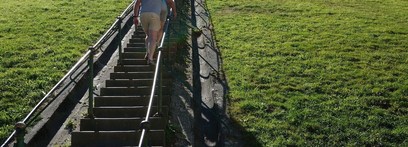 A person climbing a steep staircase on a grassy hill under a clear sky.