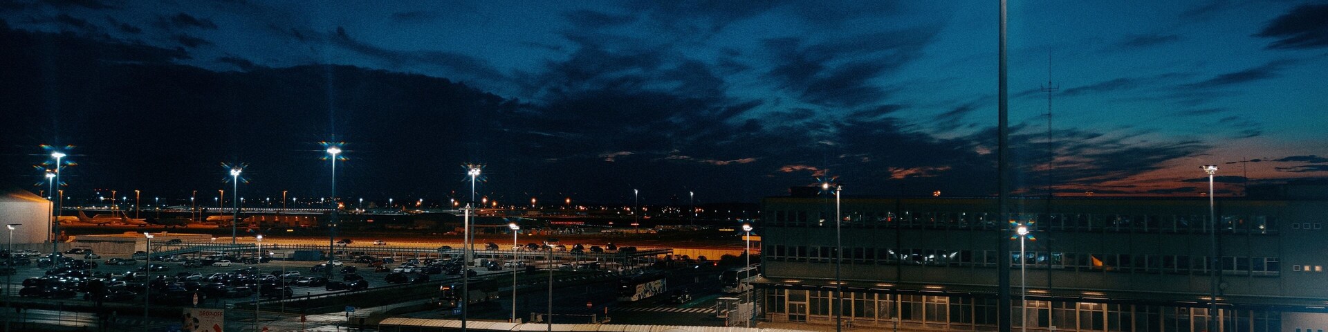 A parking lot at dusk with streetlights and a distant cityscape.