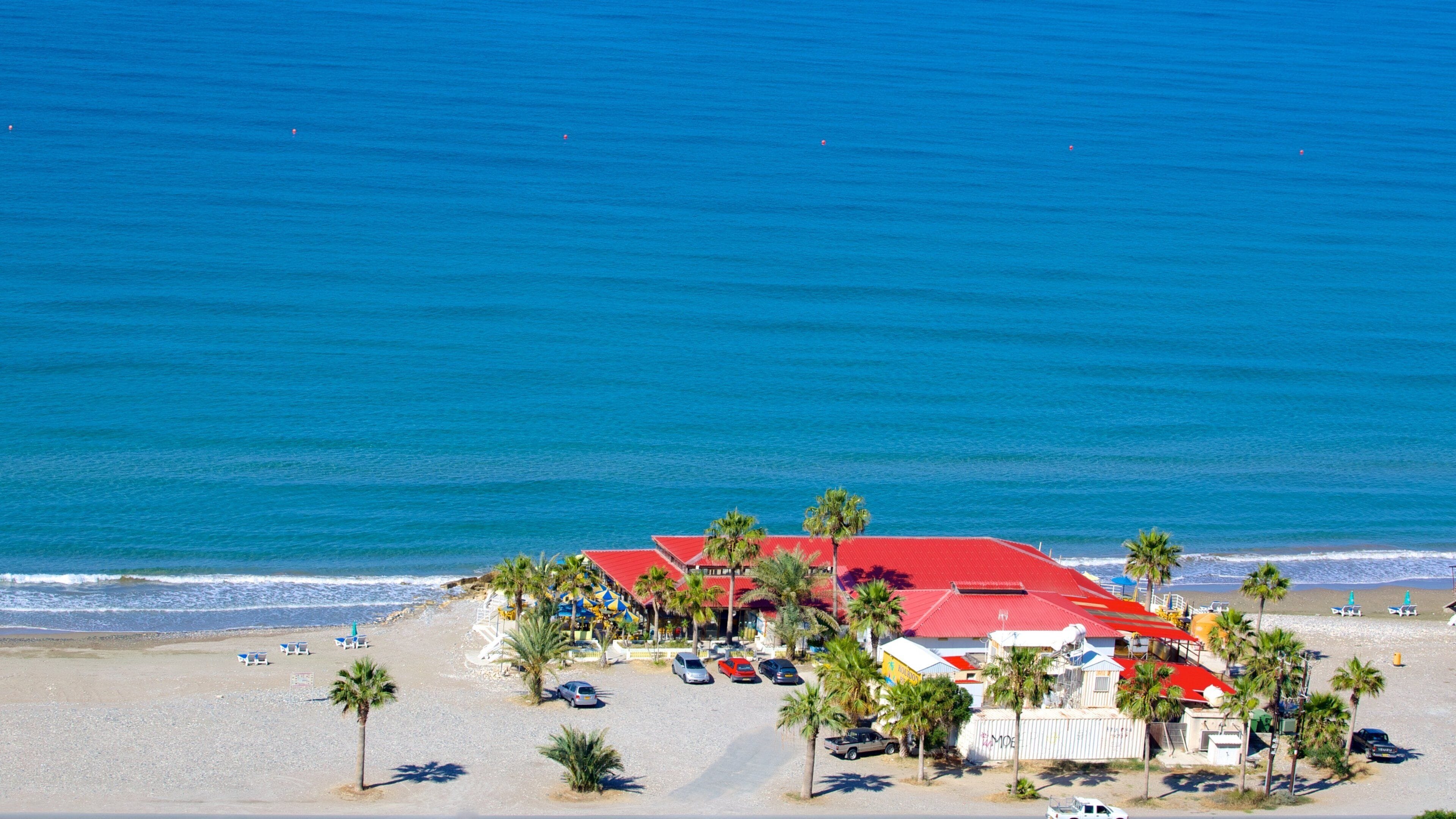 Un resort frente al mar con un edificio de techo rojo, palmeras y un océano azul cristalino.