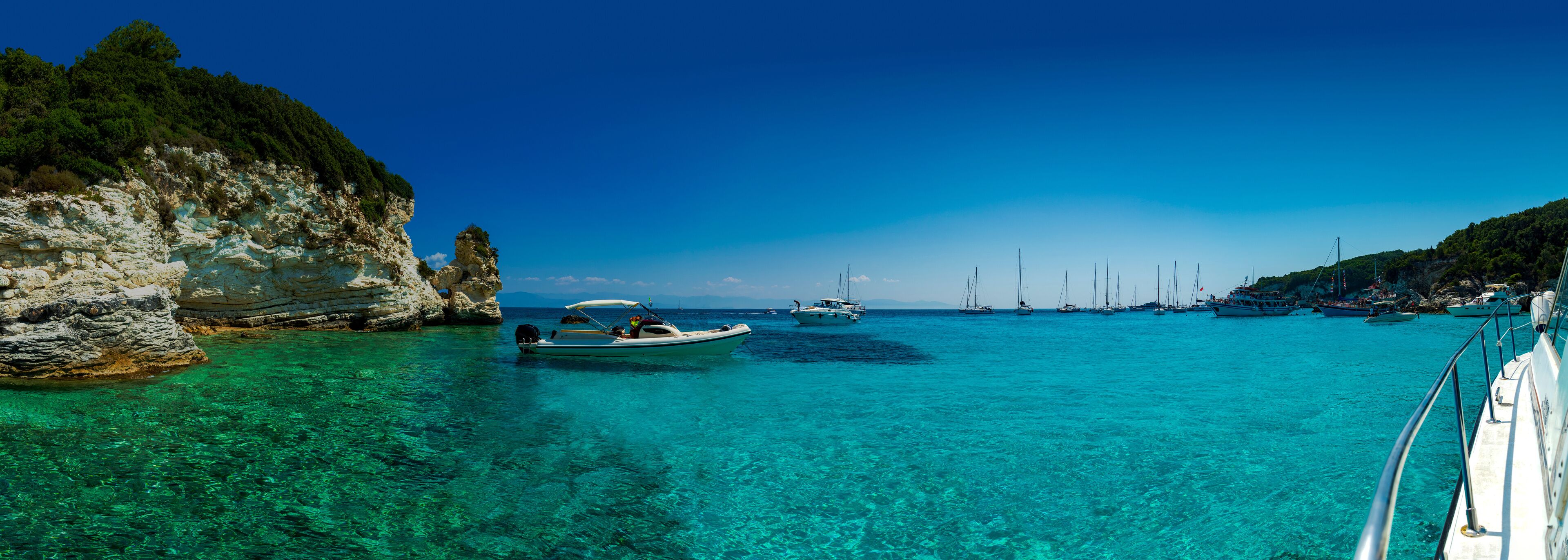 A coastal scene with clear turquoise waters, rocky cliffs, and several boats anchored near the shore.