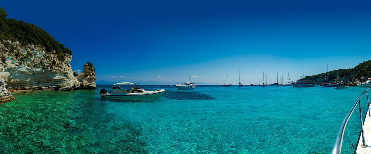 A coastal scene with clear turquoise waters, rocky cliffs, and several boats anchored near the shore.