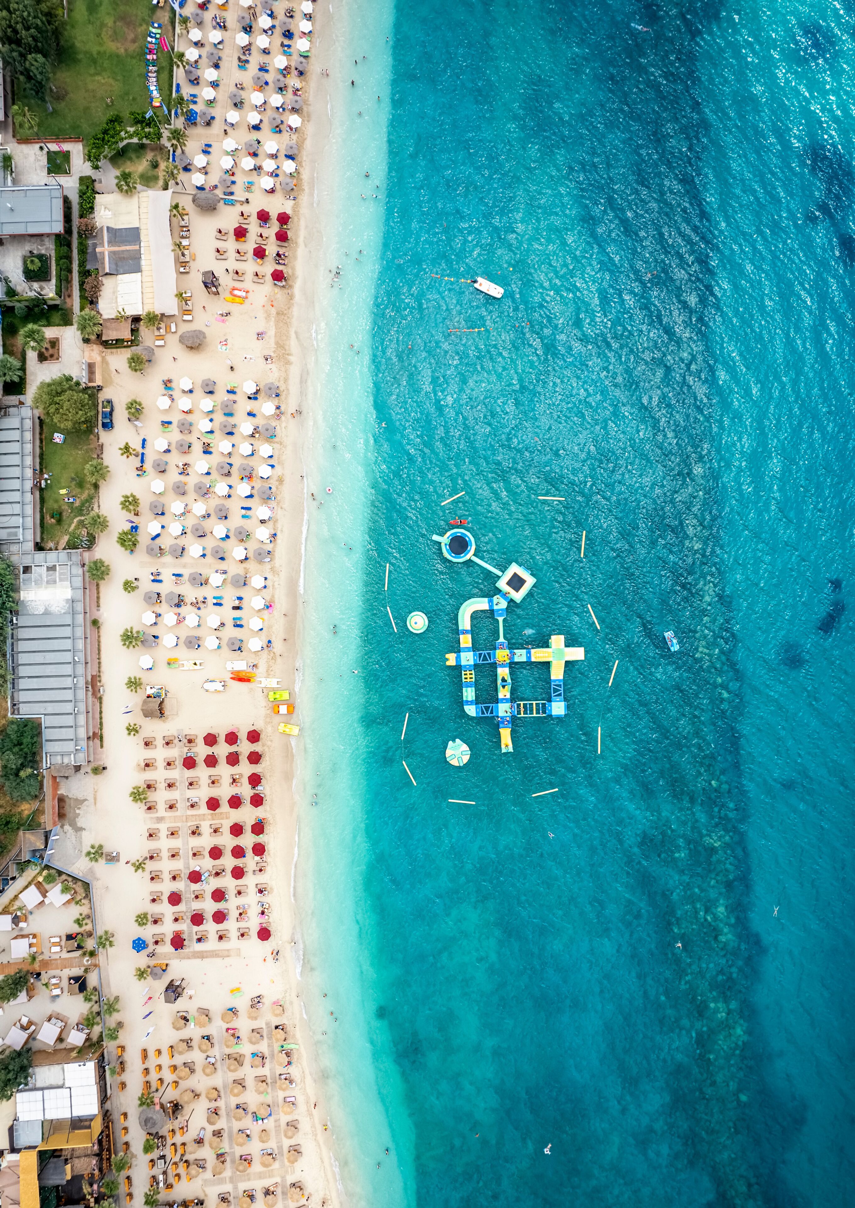 A beach with clear turquoise water, rows of umbrellas, and a boardwalk.