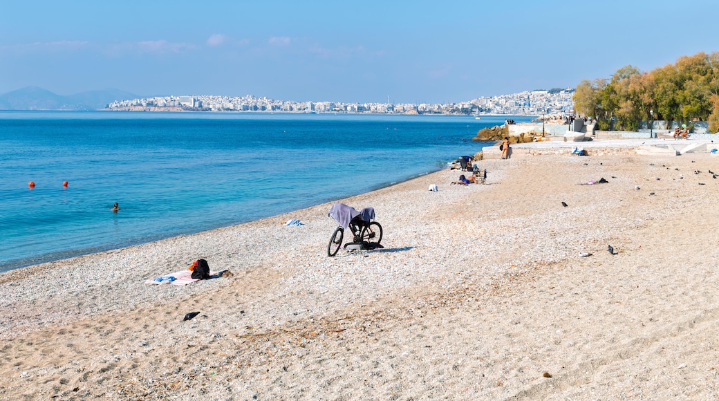 A sandy pebble beach along the Aegean Sea at the promenade of Flisvos along the Athenian Riviera with Piraeus city behind, in Palaio Faliro, Greece.