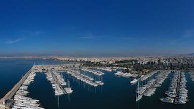 Vista aérea de um porto com inúmeros barcos atracados, rodeado por uma paisagem urbana costeira e montanhas ao fundo.