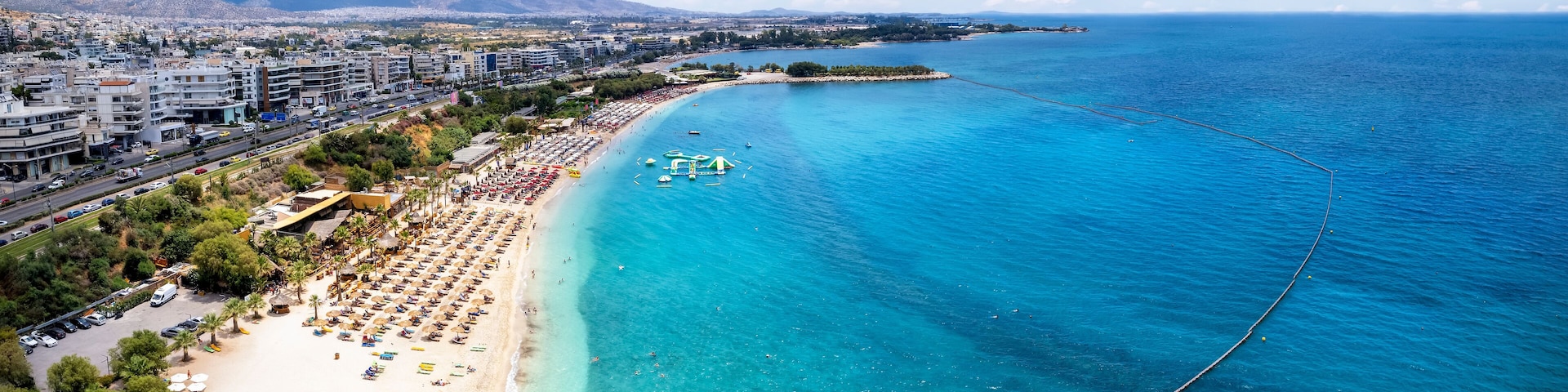 A coastal city with a beach, clear blue waters, and a mountainous backdrop.