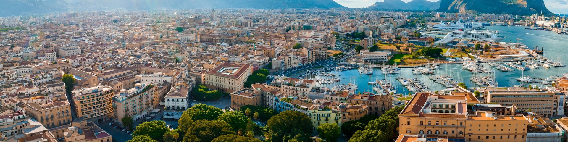 A coastal cityscape with a marina, historic buildings, and mountains in the background.