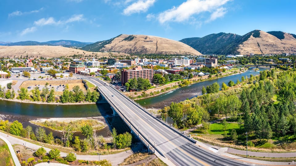 A bridge over a river, a town with buildings, and mountains in the background.