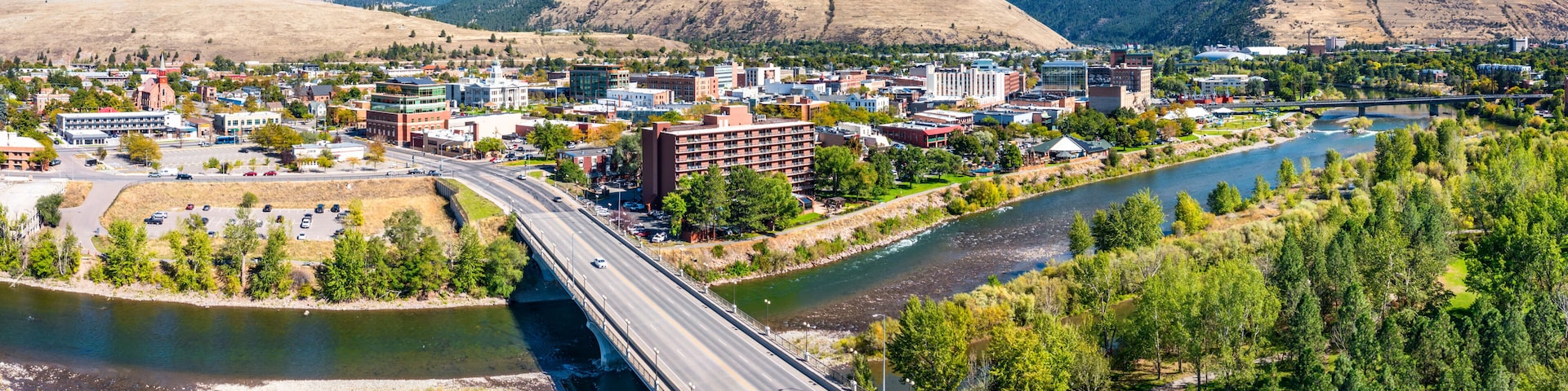 Eine Brücke über einem Fluss, eine Stadt mit Gebäuden und Berge im Hintergrund.