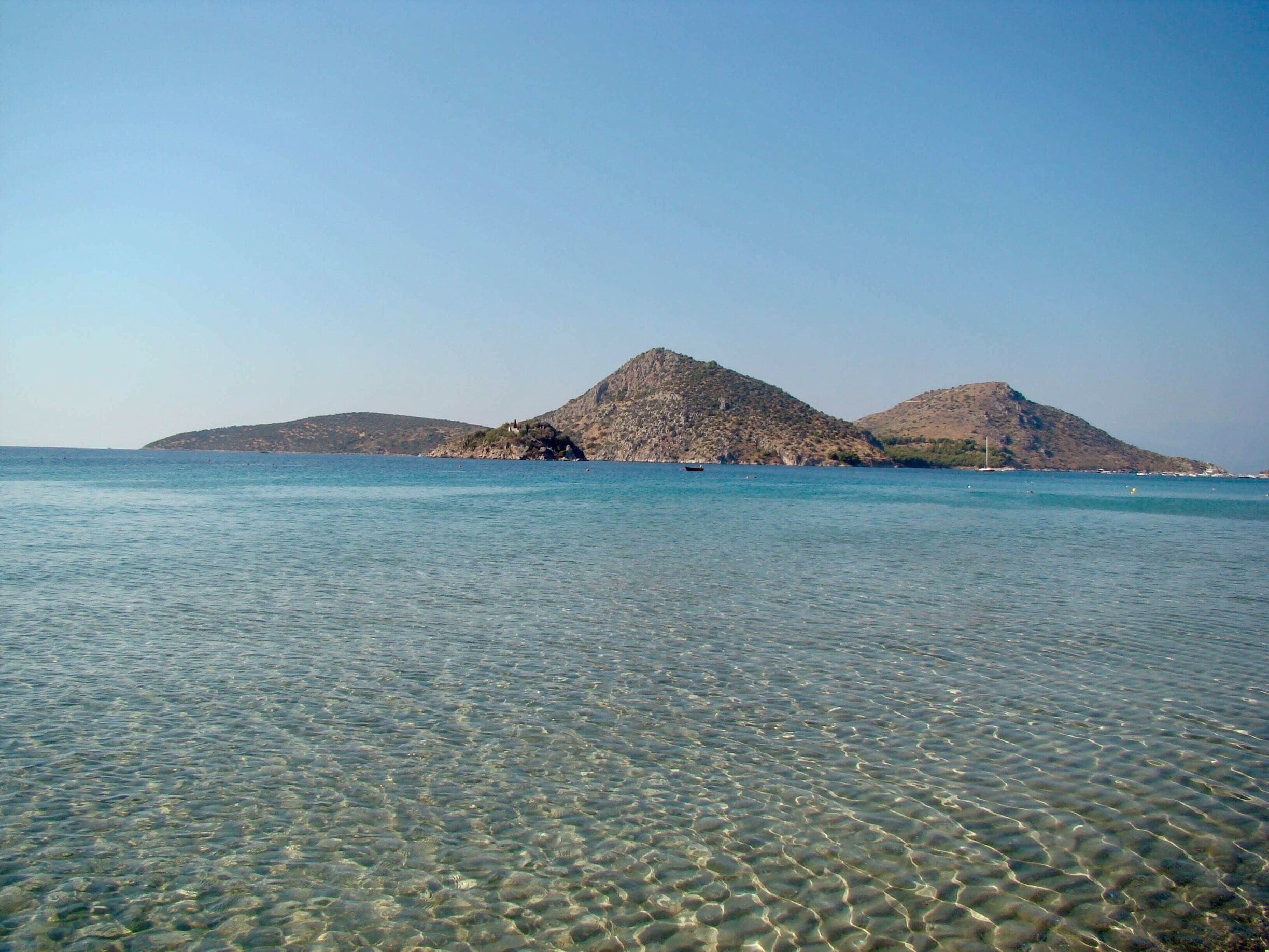 A clear coastal area with shallow water and two prominent hills in the background.