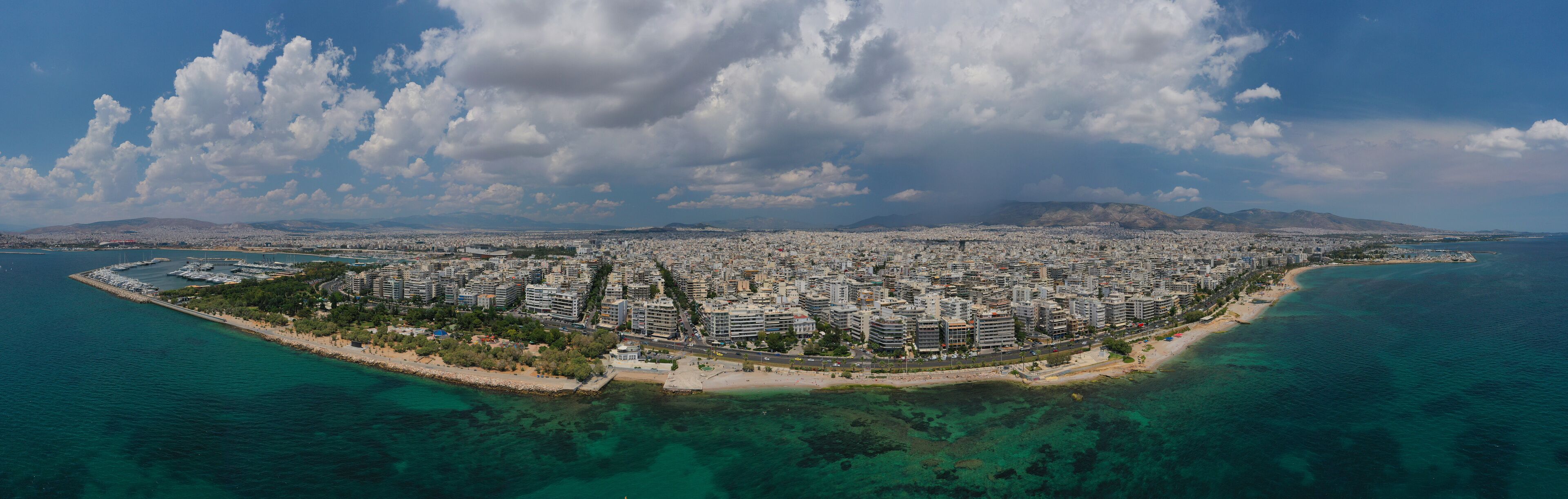 An aerial view of a coastal city with a dense urban area, a beach, and clear blue waters.